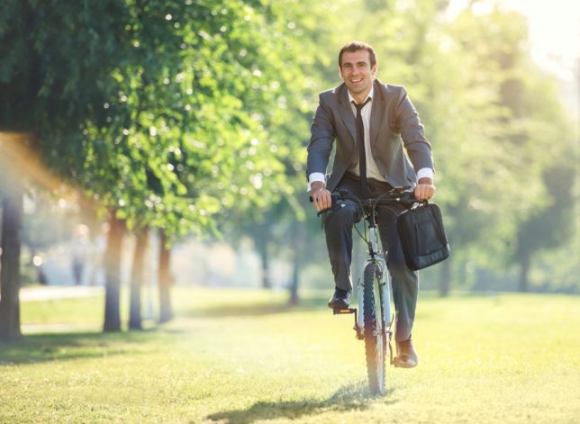 Smiling businessman riding bicycle in the park.